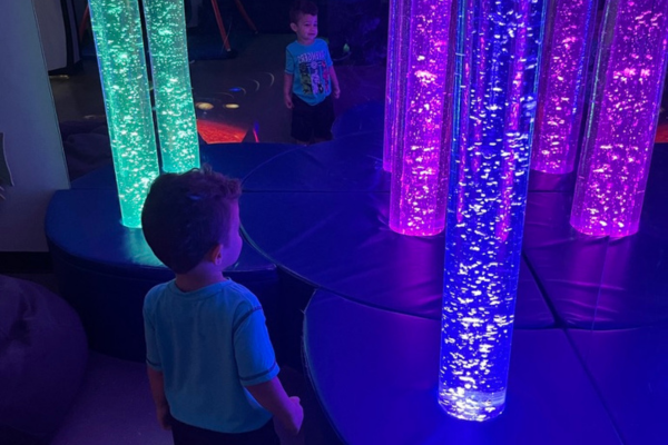 Image: A child with sensory needs is mesmerized by tall sensory tube lighting in a calming room in the science museum.