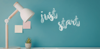 Image: A desk with a wooden desk lamp and the words "Just Start" written on a wall in the background