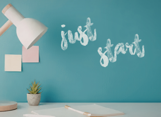 Image: A desk with a wooden desk lamp and the words "Just Start" written on a wall in the background