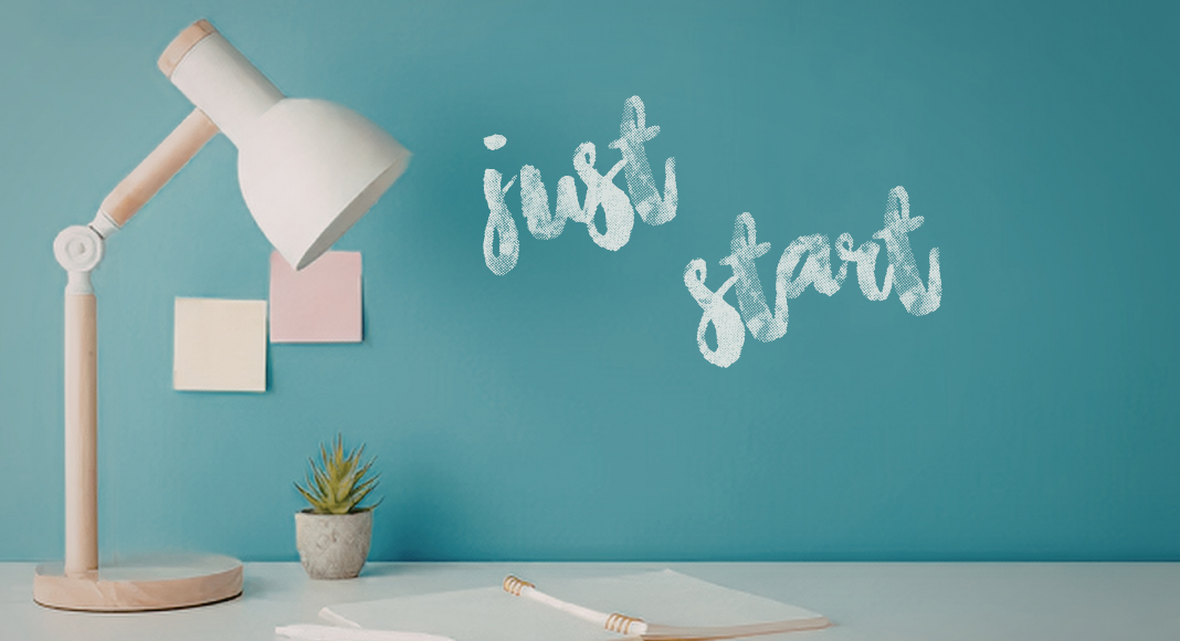 Image: A wooden desk lamp on a desk, with the text "Just Start" pained on a wall in the background