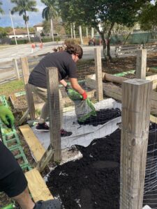 Image: Someone lays weed barrier fabric and layers it with garden soil