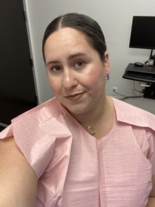 Image: A woman in a pink paper gown waiting for a diagnosis