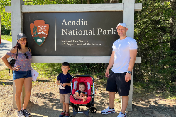 Image: A family poses for a photo in front of a sign for Acadia National Park