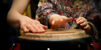 Image: A parent plays a bongo drum with their young child