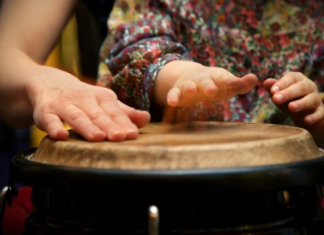 Image: A parent plays a bongo drum with their young child