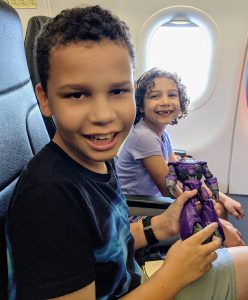 Image: Two kids smiling from their seats on an airplane