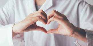 Image: A doctor in a white lab coat makes a heart with their hands