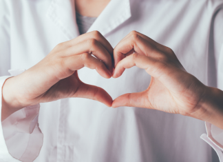Image: A doctor in a white lab coat makes a heart with their hands