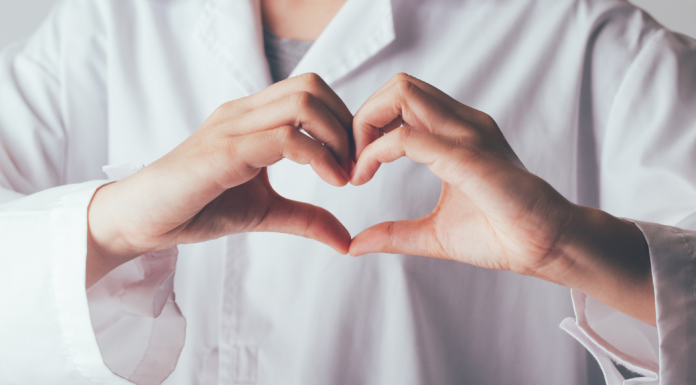 Image: A doctor in a white lab coat makes a heart with their hands