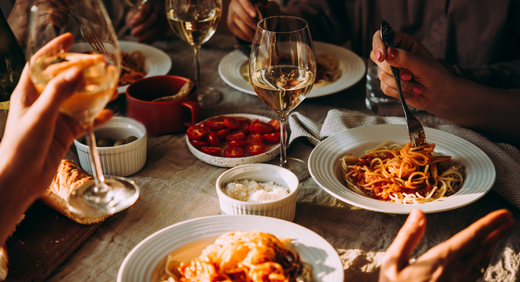 Image: A group of people enjoy a meal of pasta and wine