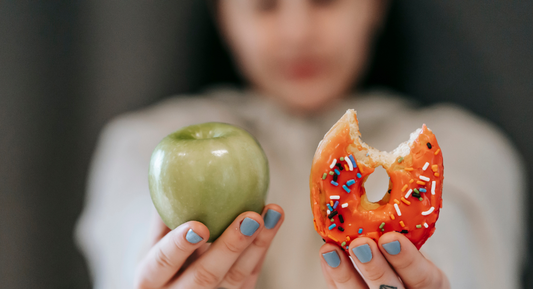 Image: A woman holds an apple in one hand and a donut in the other
