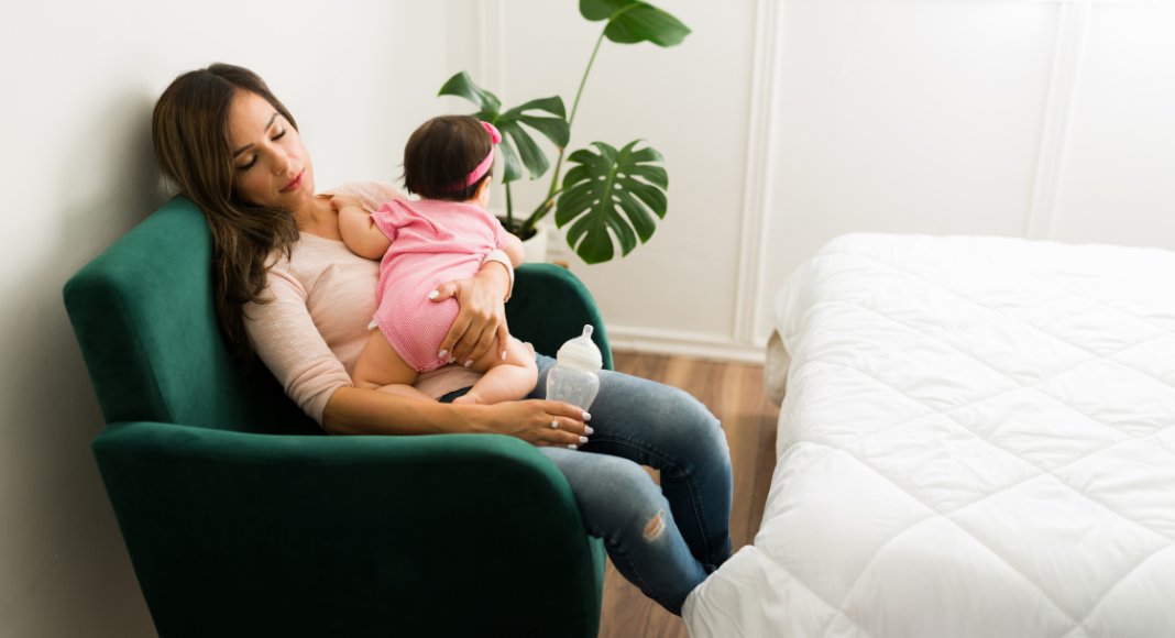 Image: A mother naps in a chair while holding a baby in her lap