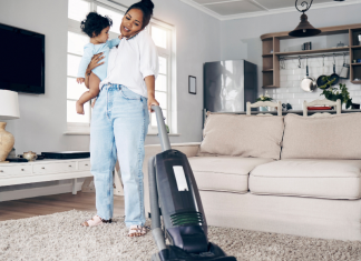 Image: A mom vacuums while holding a toddler