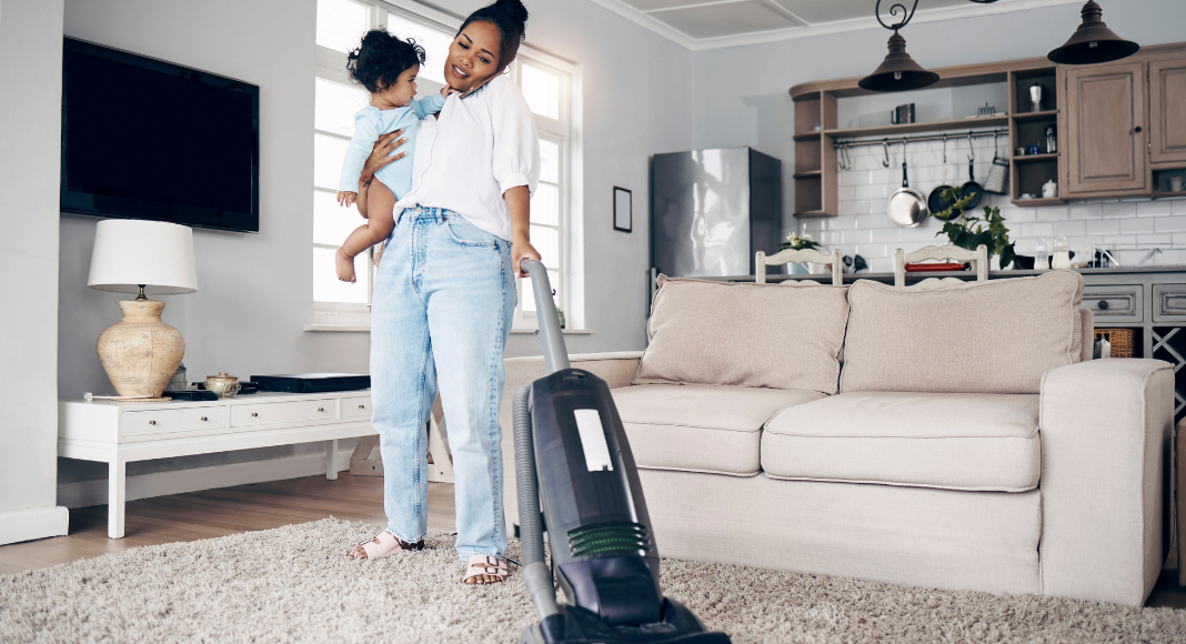 Image: A mom vacuums while holding a toddler