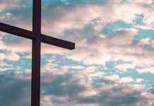 Image: A large cross silhouetted against a cloudy daytime sky