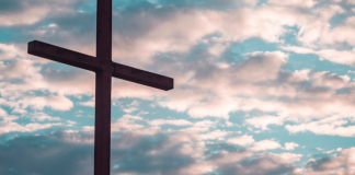 Image: A large cross silhouetted against a cloudy daytime sky