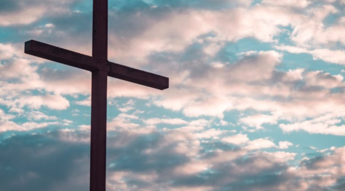 Image: A large cross silhouetted against a cloudy daytime sky