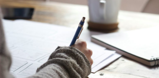 Image: Someone sitting at a desk with a pen in their hand and a cup of coffee in the background
