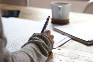 Image: Somone witting at a desk with a pen in their hand and a cup of coffee
