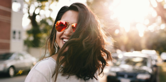 Image: A confident woman wearing sunglasses and smiling as she crosses the street