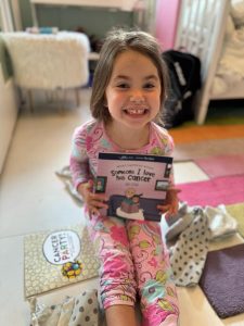 Image: A little girl holds a book titled, Someone I Know Has Cancer