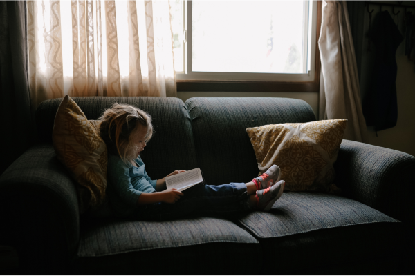 Image: A little girl sitting on a couch and reading a book