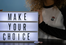 Image: A woman with an "I voted" sticker holds a letterboard that reads, "Make Your Choice"