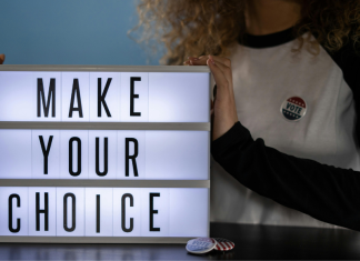 Image: A woman with an "I voted" sticker holds a letterboard that reads, "Make Your Choice"