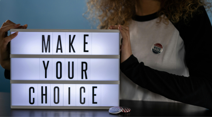 Image: A woman with an "I voted" sticker holds a letterboard that reads, "Make Your Choice"