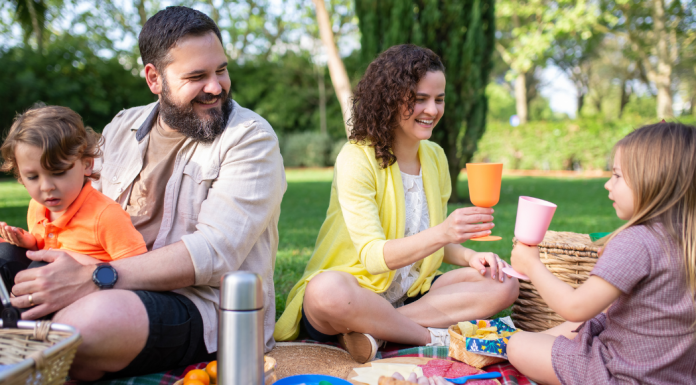 2024 Summer Bucket List {With Printable!} Image: A family enjoys an outdoor picnic at the park