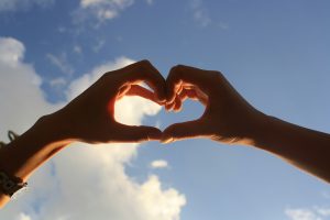 Image: Two hands forming a heart with the sky in the background