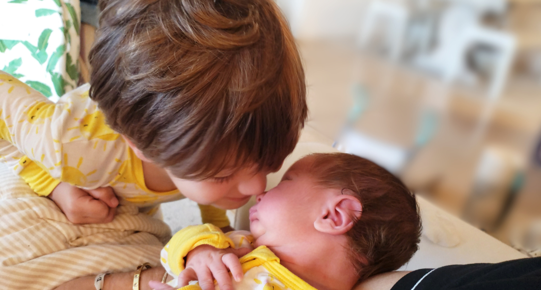 Image: A young boy looks lovingly at his newborn baby brother