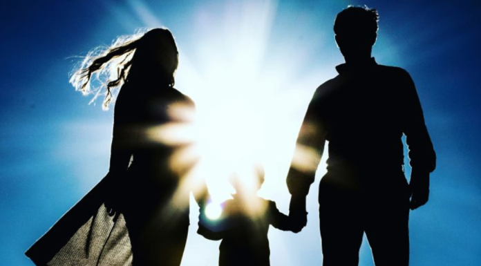 Image: A silhouette of a family holding hands against a blue sky