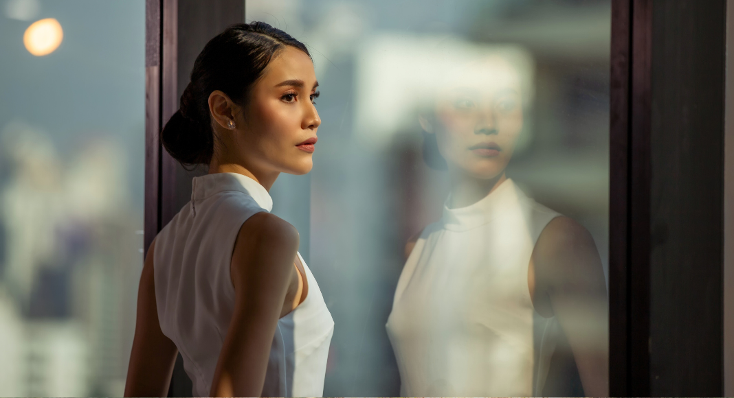 Image: A corporate woman stands at a window in an office building