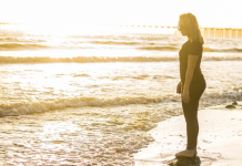 Image: A woman standing on the shoreline, watching the waves