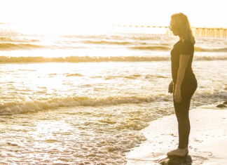 Image: A woman standing on the shoreline, watching the waves