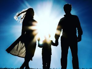 Image: A silhouette of a family holding hands against a blue sky