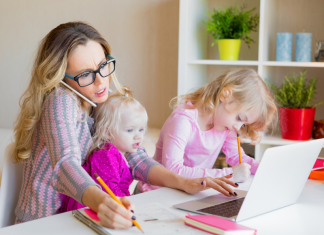 Image: A working mom trying to work from home with a toddler on her lap and a preschooler next to her