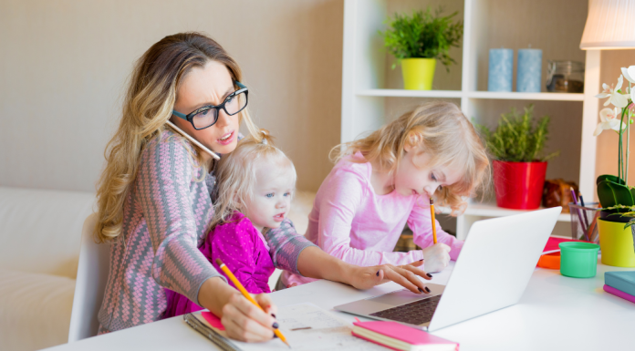 Working Mom Dilemma: Finding Balance in a Fast-Paced World Image: A working mom trying to work from home with a toddler on her lap and a preschooler next to her