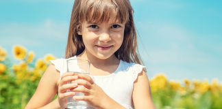 Fluoride: Benefits, Risks & Cavity Prevention in Children | Dr. Bob Image: A little girl holds a glass of tap water with a sunflower field in the background