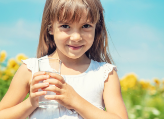 Fluoride: Benefits, Risks & Cavity Prevention in Children | Dr. Bob Image: A little girl holds a glass of tap water with a sunflower field in the background