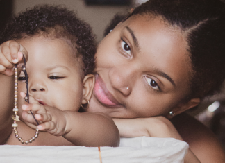 Image: A Black mother smiles while her infant plays
