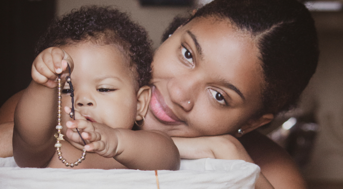 Image: A Black mother smiles while her infant plays