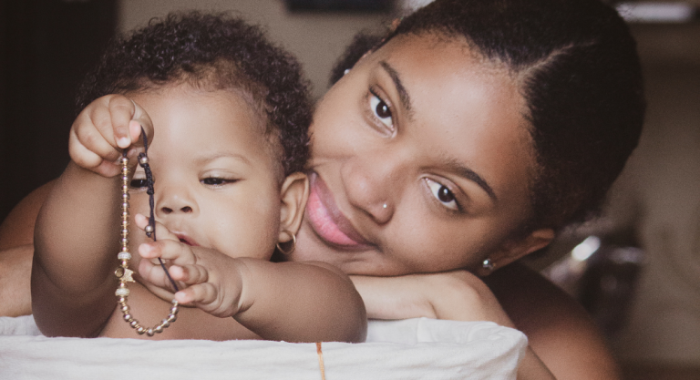 Image: A Black mother smiles while her infant plays