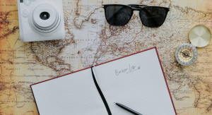 Image: A camera, sunglasses, compass, and journal spread across a map
