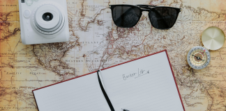 Image: A camera, sunglasses, compass, and journal spread across a map