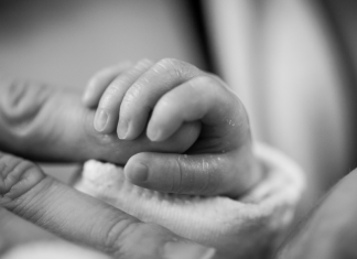 A premature infant holds onto a parent's finger