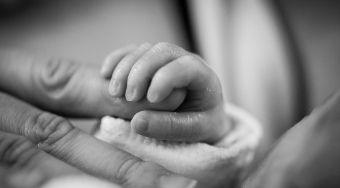 A premature infant holds onto a parent's finger