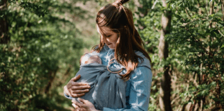 A postpartum mom wearing her newborn baby in a sling