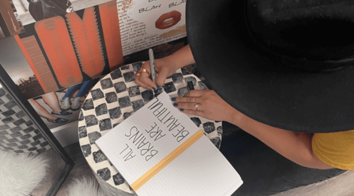 A woman writing in a journal that reads, "All brains are beautiful," a statement of support for neurodiversity